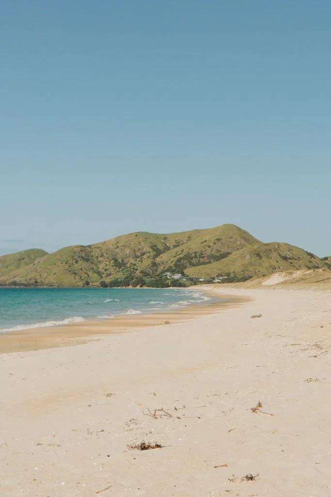 A beach with soft almost pink sand arcs around to a low headland