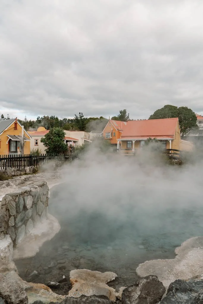 A steaming blue hot pool in front of yellow and orange houses