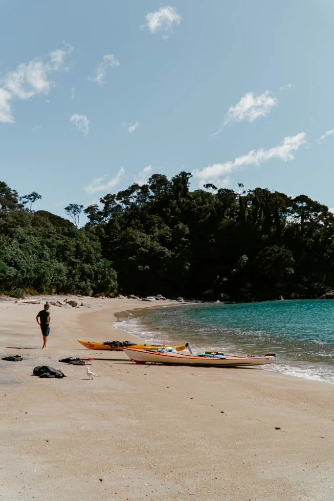 A man stands with his hands on his hips looking at two kayaks pulled up on the beach