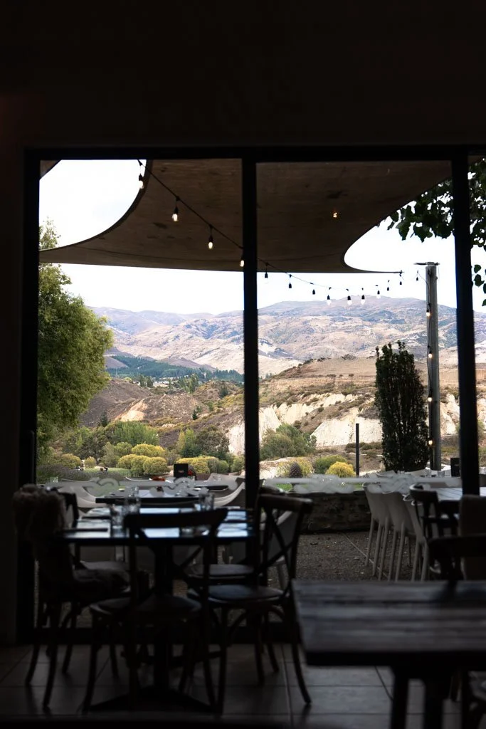 Brown hills and vines are visible beyond seating and a marquee with festoon lights at Carrick Winery