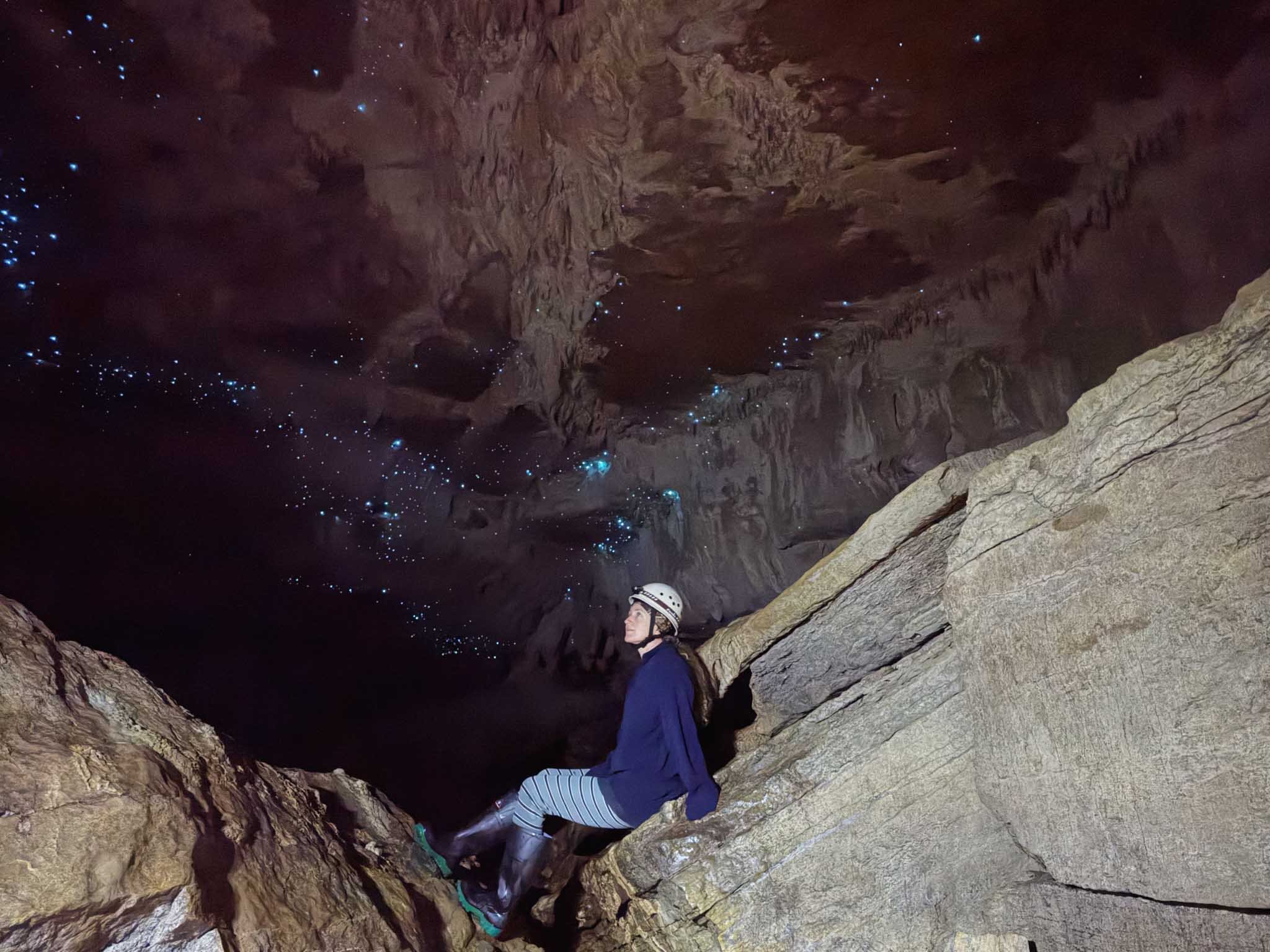 A woman looks up at a cave ceiling in Waitomo, with glow worms scattered across it