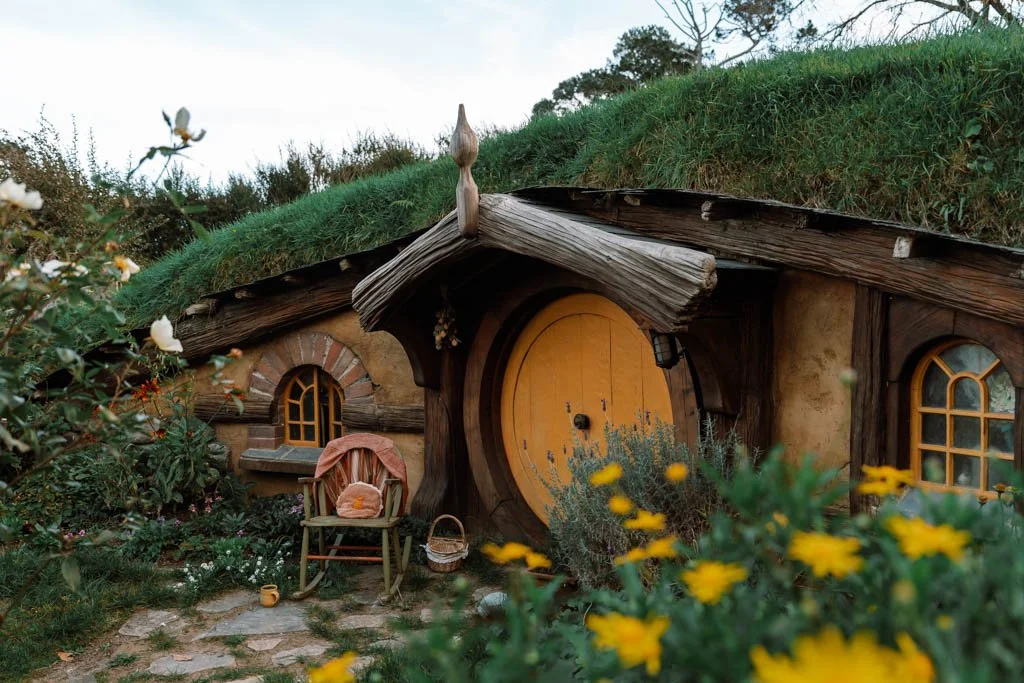 A hobbit hole with a yellow door and a small rocking chair beside it in Hobbiton, New Zealand