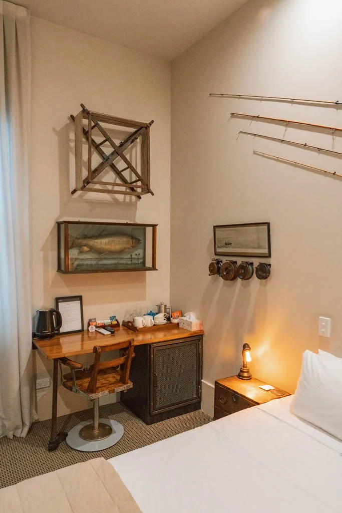 A hotel room has fly fishing rods on the wall, alongside a fish mounted in a box