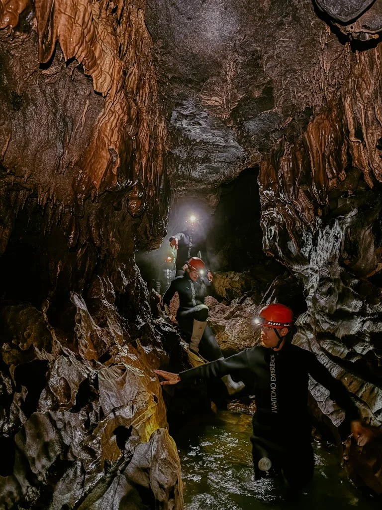 People in red helmets with torches on the front climb through caves