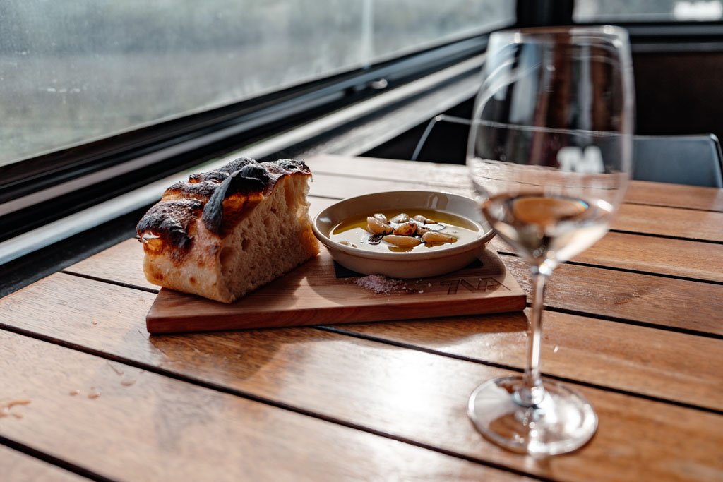 A plate of bread and olive oil sits next to a glass of Te Motu wine
