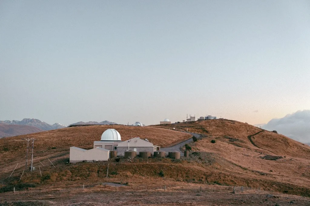The white rounded roofs of the Mount John Observatory in Lake Tekapo stand in contrast against golden hills