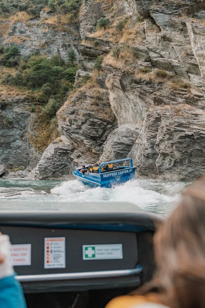A blue jet boat whips up a river in a canyon near Queenstown