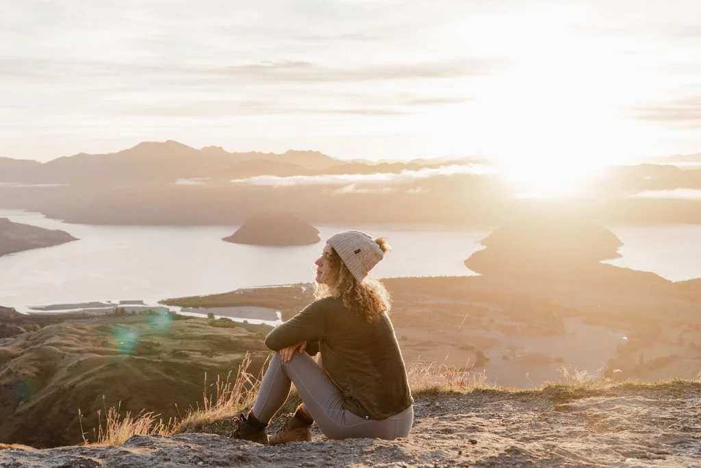 A woman sits at a viewpoint of a lake, bathed in morning glow