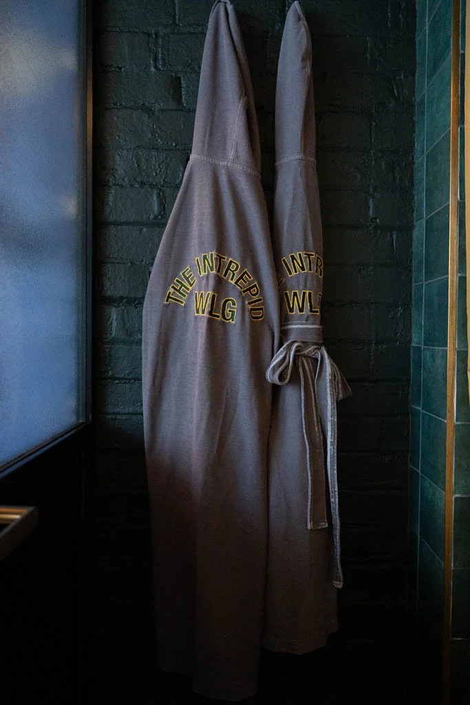 Robes with Intrepid Hotel Wellington written on the back hang against a green tiled wall