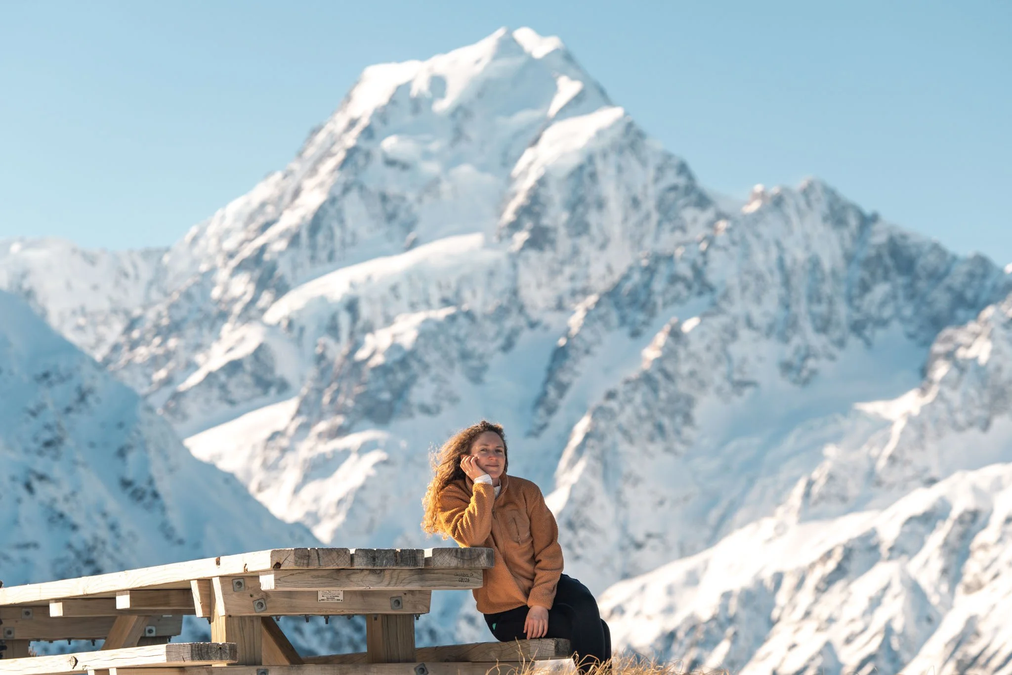 A woman sits at a table with a view of Mount Cook in the background