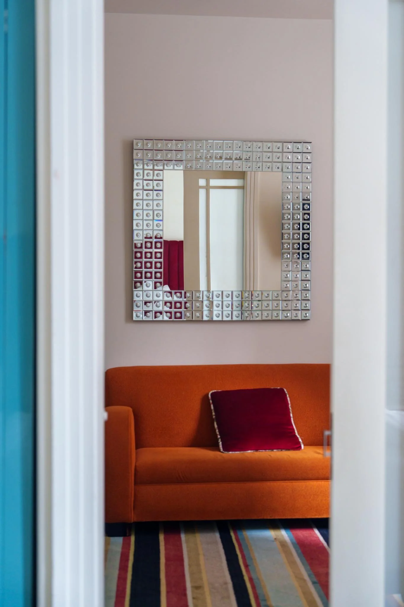 An orange sofa with a red cushion sits below an art deco textured mirror
