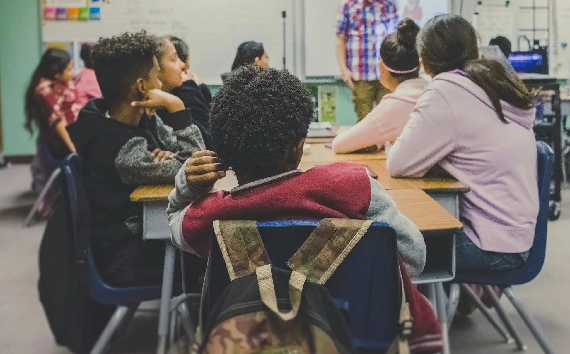 A classroom with students listening to a teacher standing in front of a whiteboard.