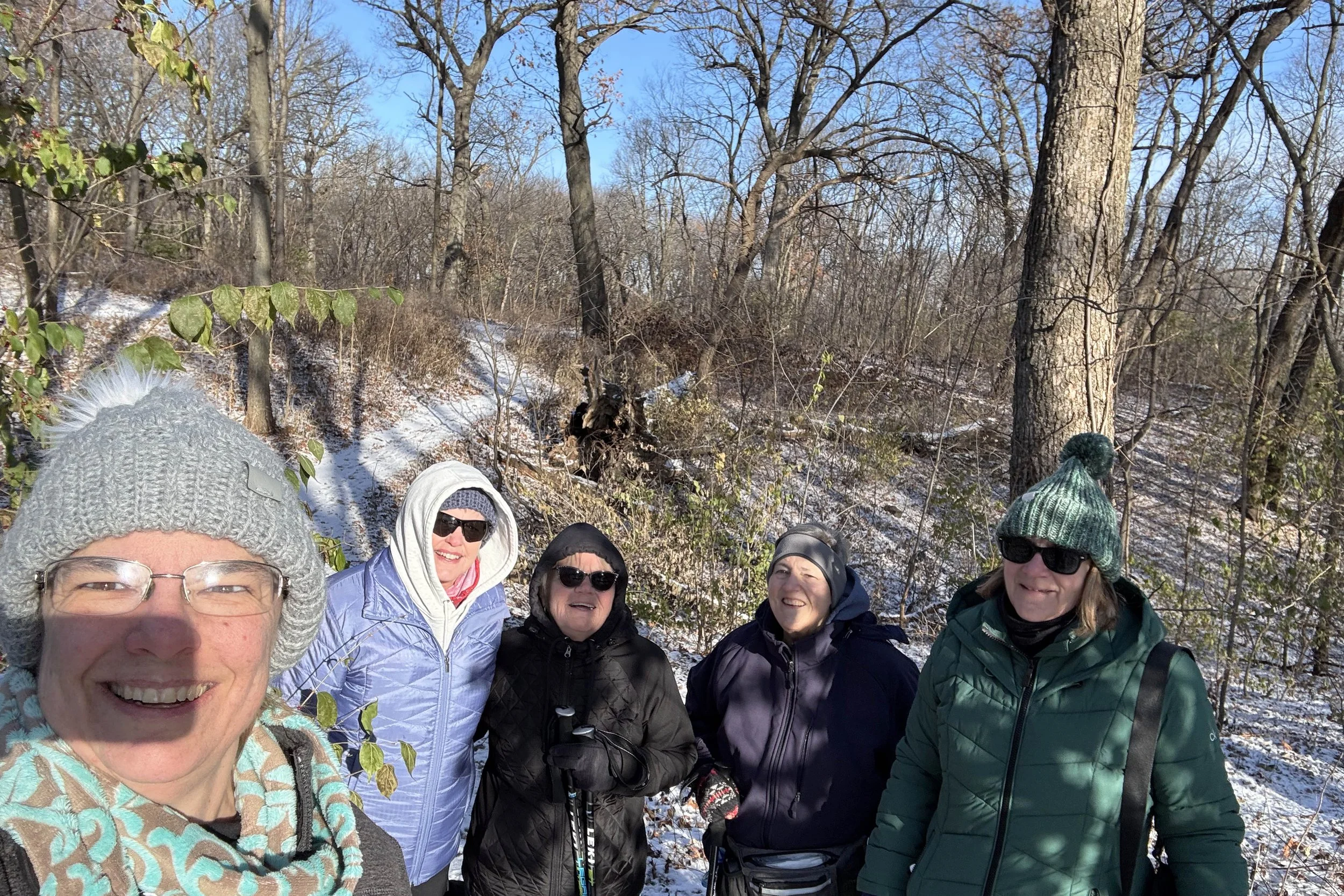 Five hikers in hats and coats pose for a photo in front of the snow covered trail.