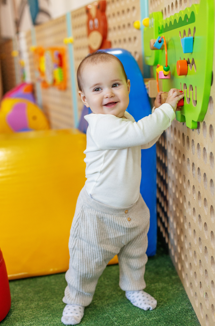 A toddler playing with a colorful wall-mounted toy in a play area.