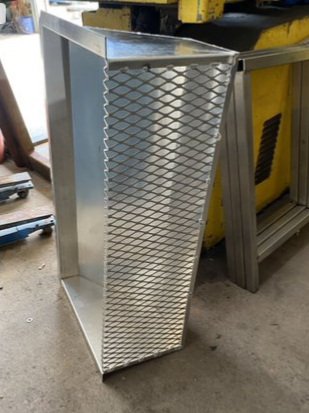 A metal duct with a diamond-pattern grille in a workshop setting.