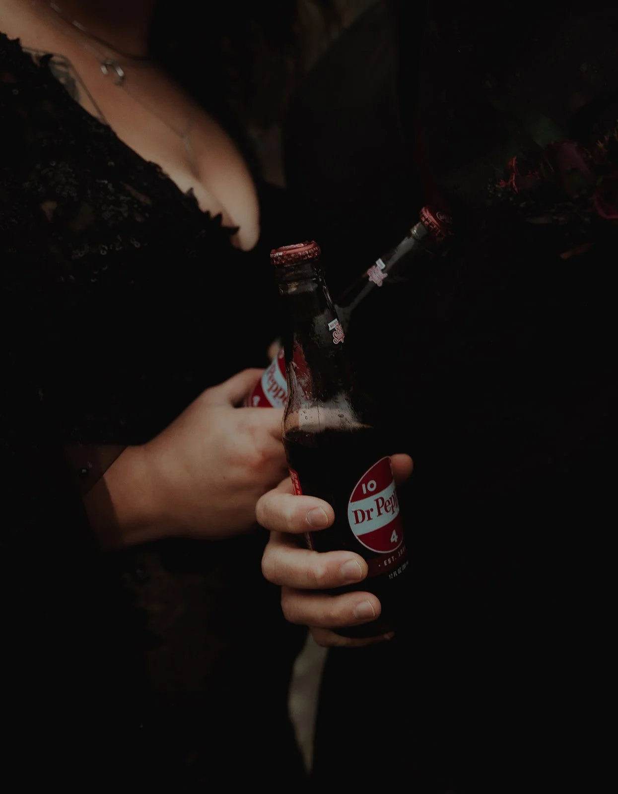 Person holding a Dr. Pepper glass bottle in a dark setting, with other bottles partially visible around.
