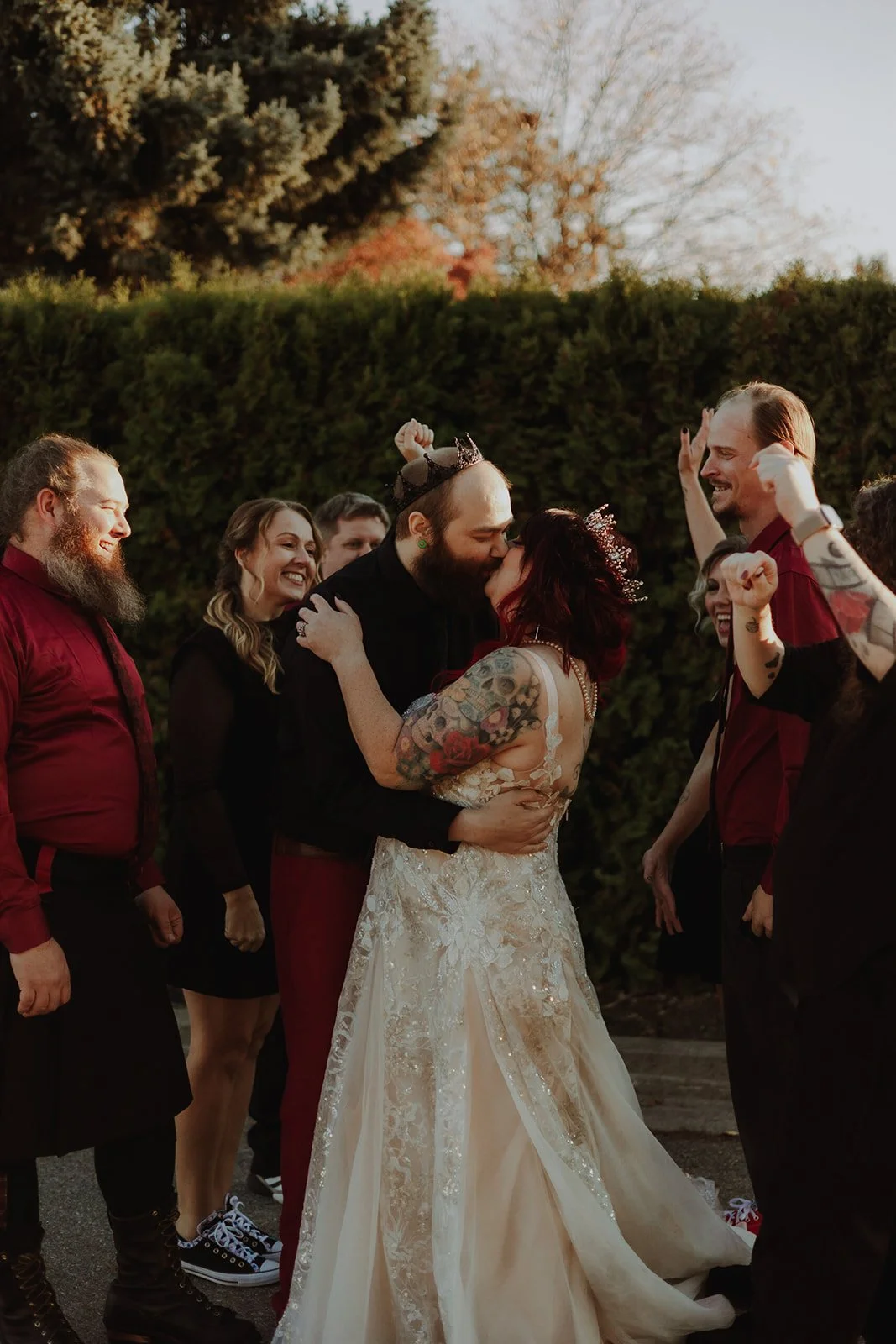A group of people celebrating at a wedding, with a couple kissing in the center, surrounded by friends smiling and raising their hands.