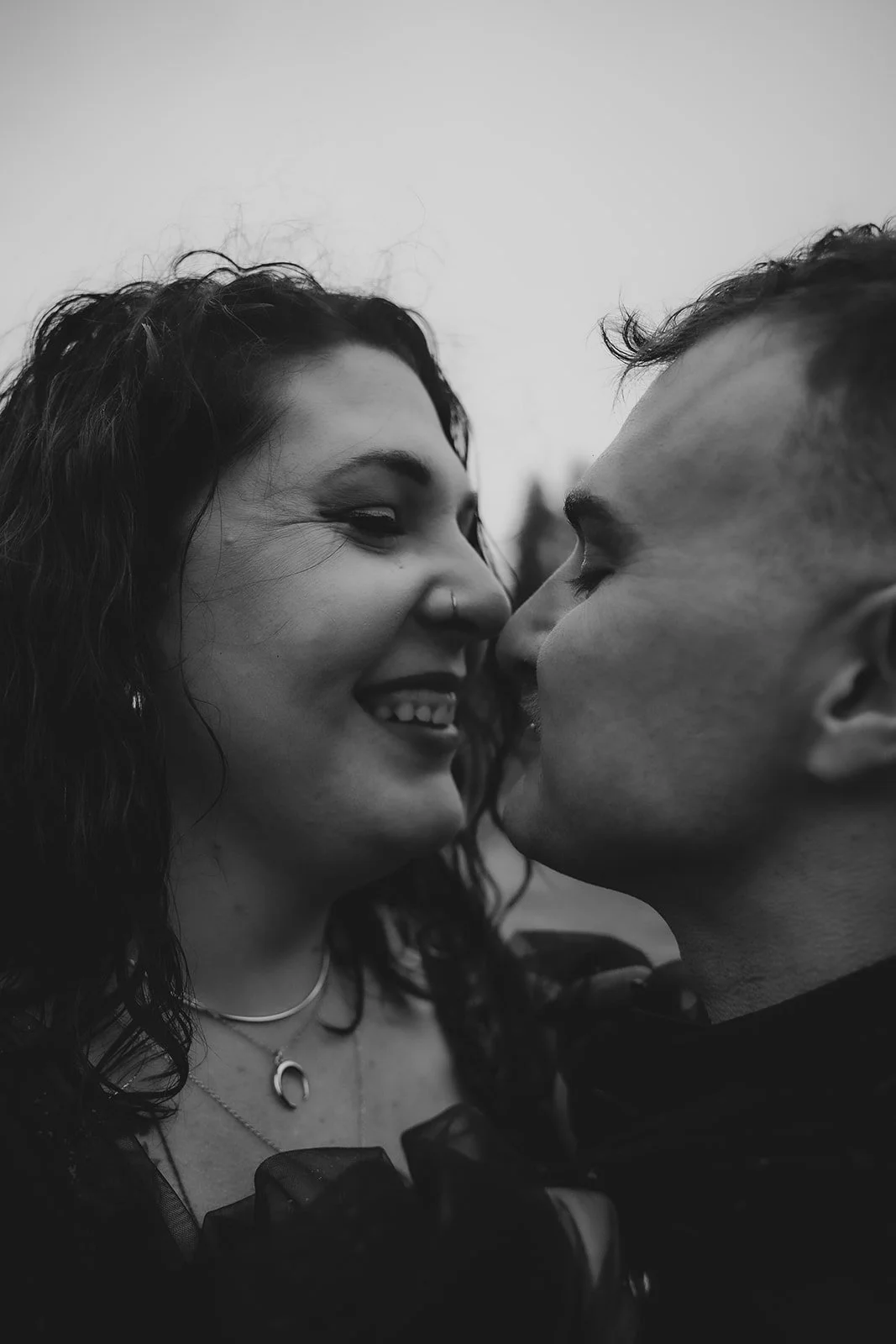 A black and white photo of a couple with their faces close, sharing a kiss and smiling.