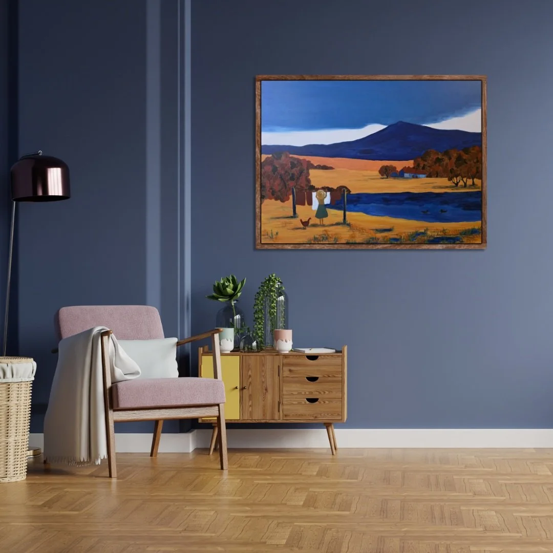 A cozy living room with a blue wall, wooden furniture, a soft chair, and the framed Silence of the Land abstract artwork painting hanging above.
