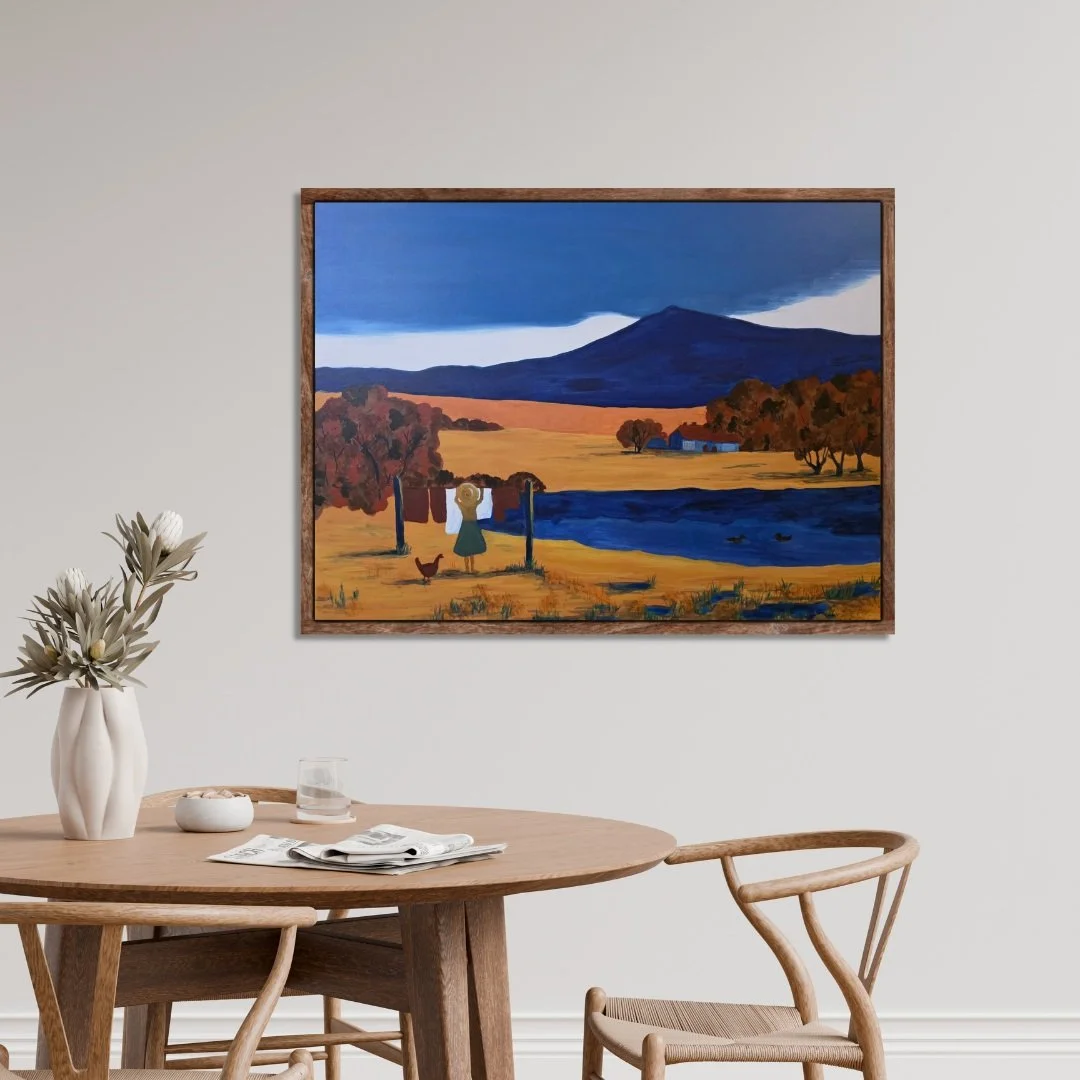 The Silence of the Land framed abstract artwork painting hangs on a light wall above a round wooden table with simple chairs and a small vase.