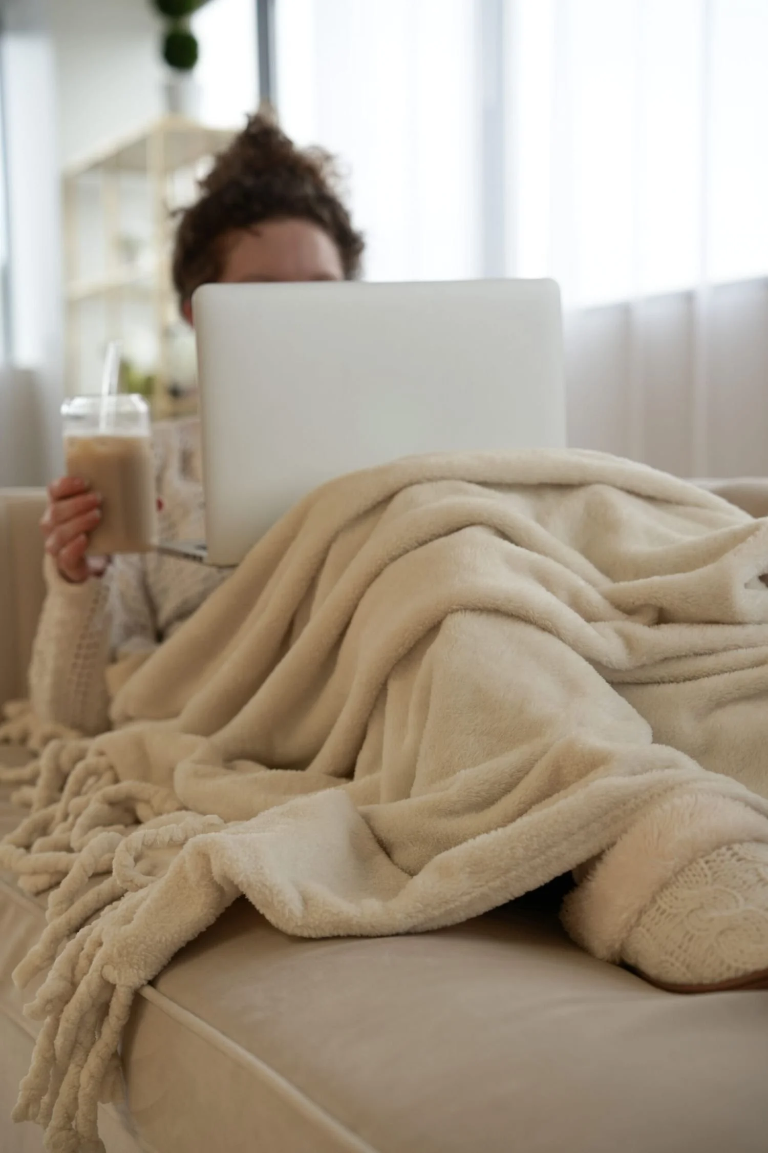 Woman sitting on a couch with a laptop and blanket during a virtual therapy session for high emotional reactivity