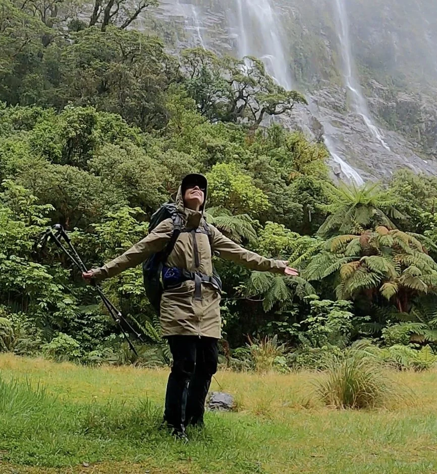 Sharon Evans dancing below magnificent waterfalls on Milford Track, Fiordland National Park, New Zealand Great Walks