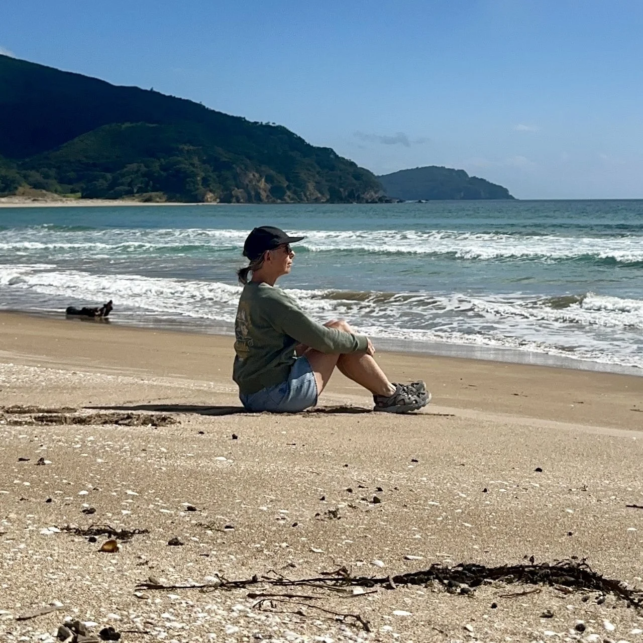 Medium shot of a woman sitting side on at the beach looking toward the horizon, reflecting on purpose and self trust