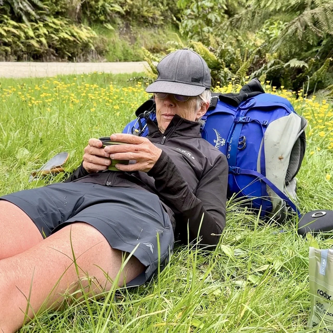 Te Araroa Hiker resting on the grass, leaning agains backpack and holding a cup of tea