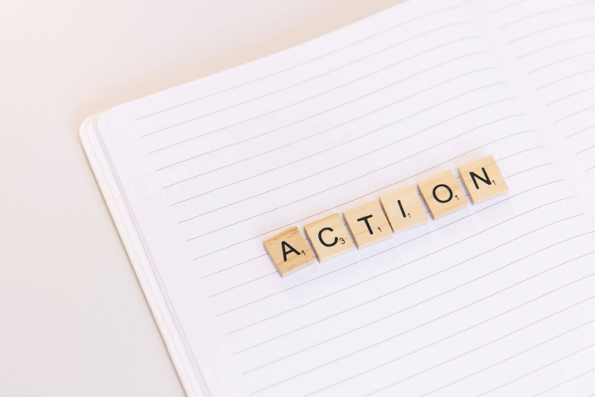 Scrabble tiles spelling 'ACTION' on an open notebook with lined pages.