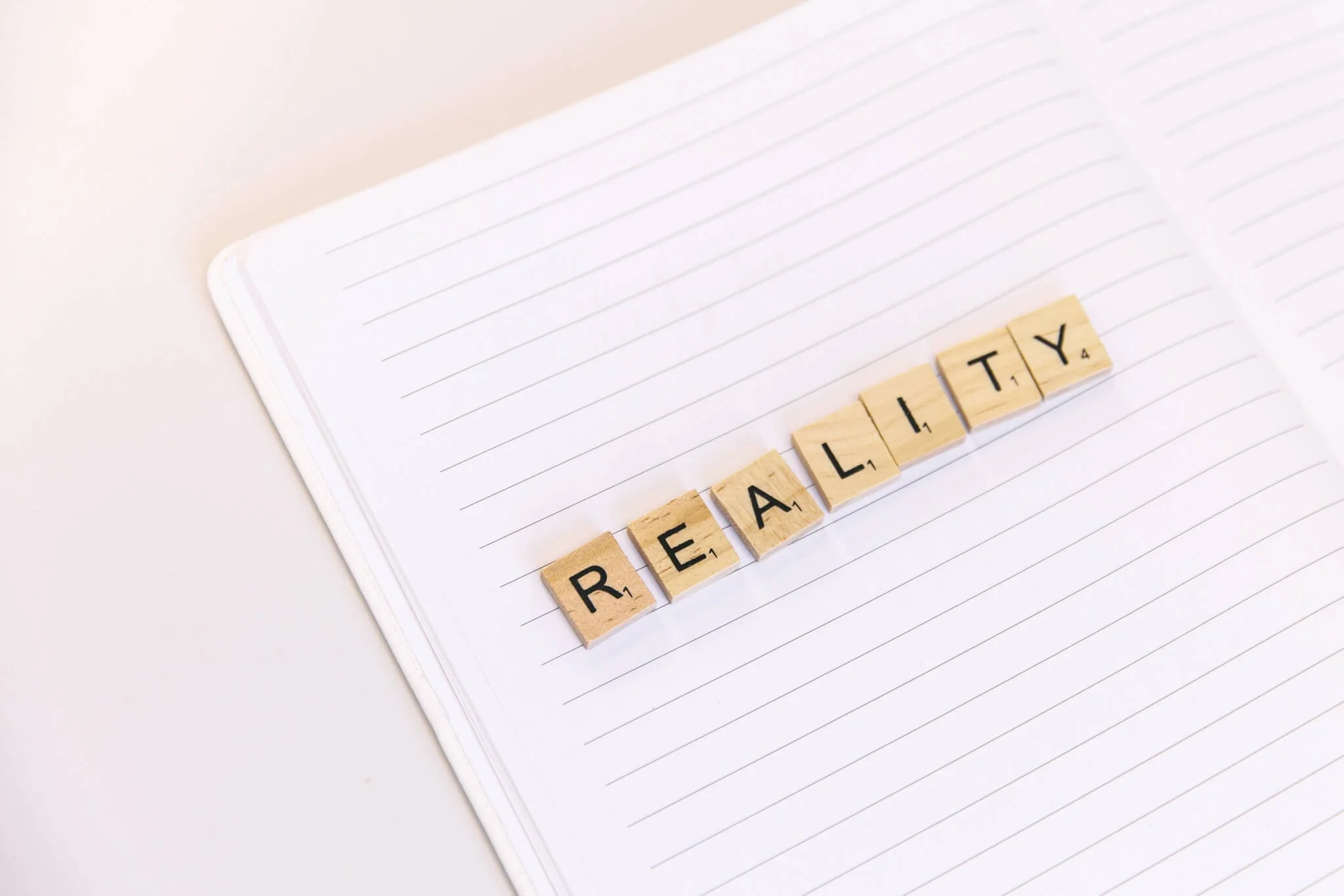 Scrabble tiles spelling 'REALTY' on a lined notebook open on a white surface.