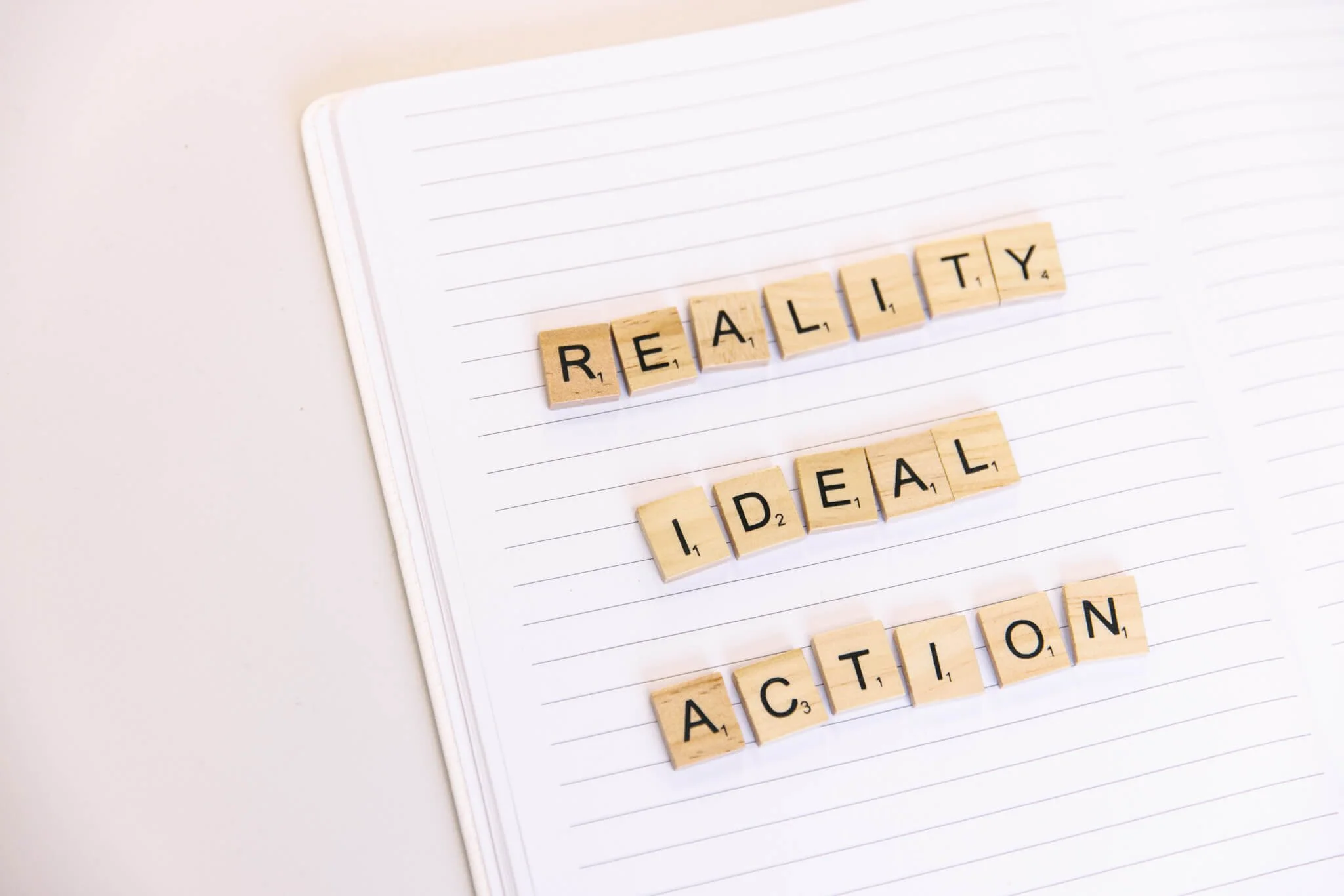 Notebook with the words 'Reality', 'Ideal', and 'Action' spelled out with Scrabble tiles.