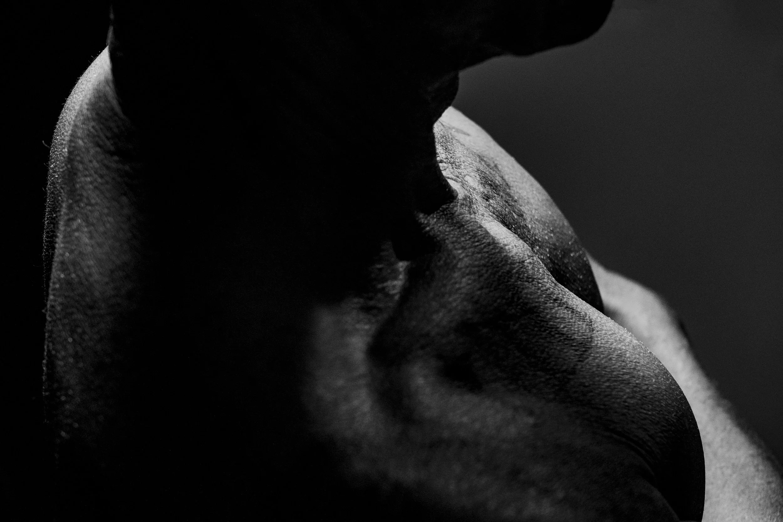 Close-up black and white photo of a person's face and shoulder, with strong shadows and textured skin features.