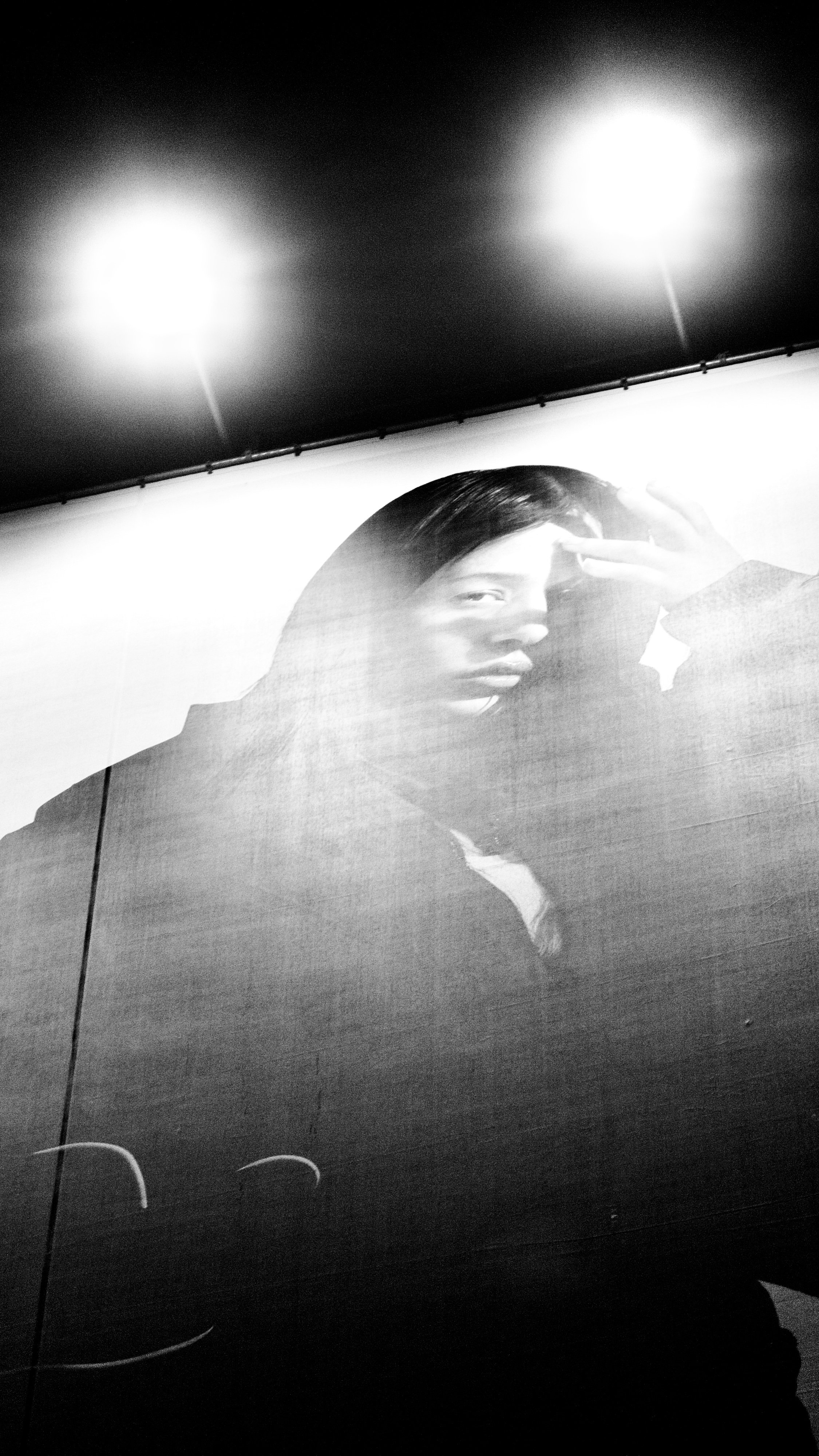 A black and white photograph of a woman with long hair looking into a mirror and taking a selfie with a phone.