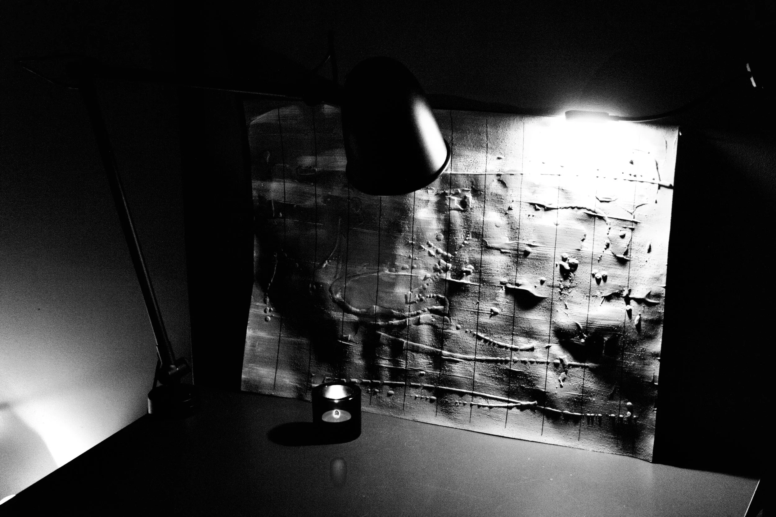 A black and white photo of a lunar surface or asteroid with craters, taken through a window with reflections of a spacecraft interior, including a cylindrical object and a light source.