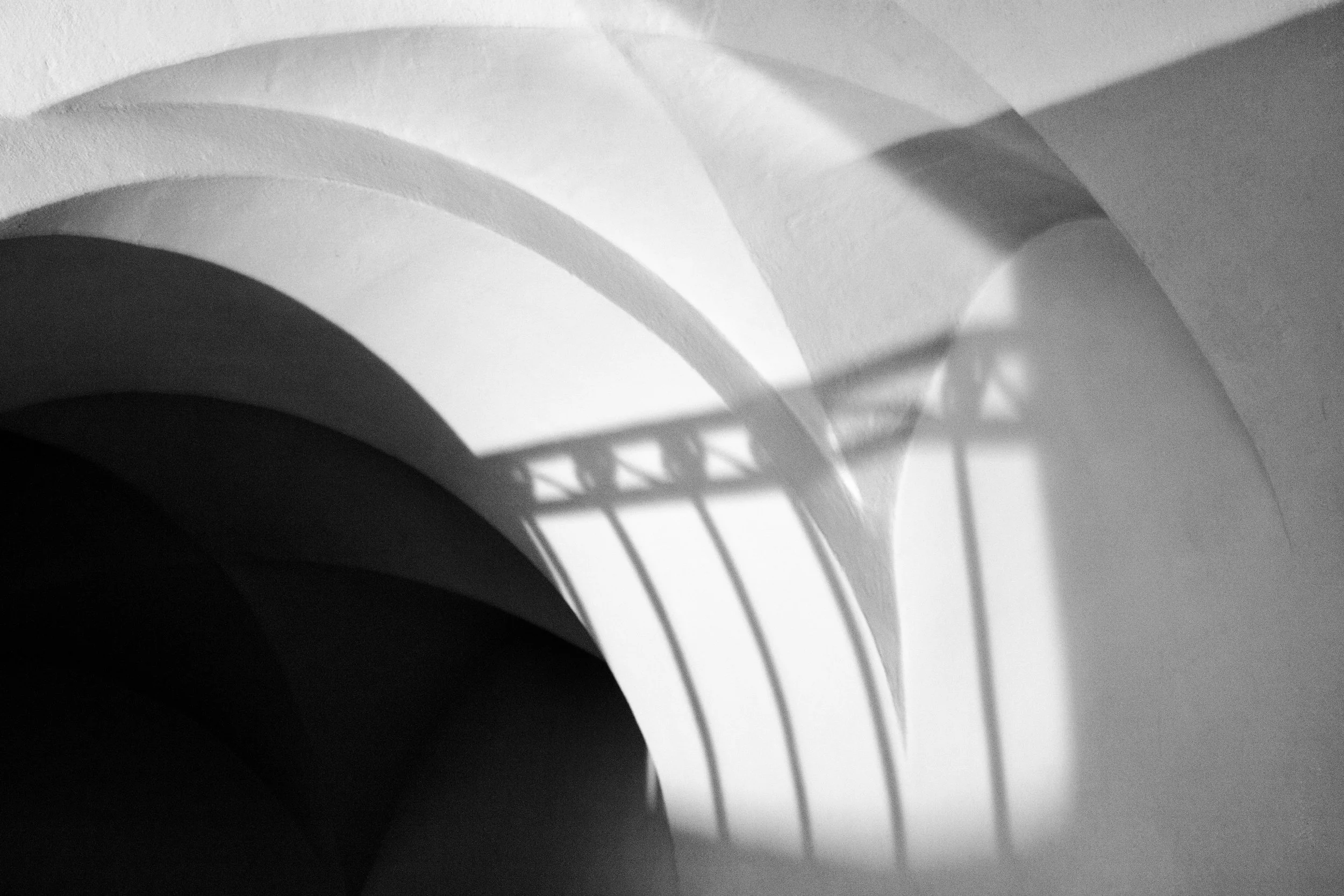 Abstract black and white image with curved, shadowed shapes and geometric light patterns.