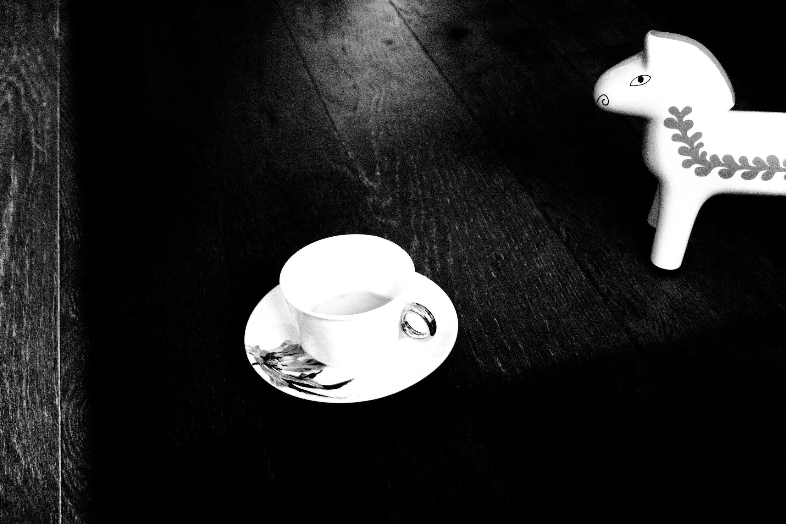 A white ceramic cup and saucer set with a floral design, a small decorative rabbit figure with a floral pattern on its side, and a small round object on a dark wooden surface.