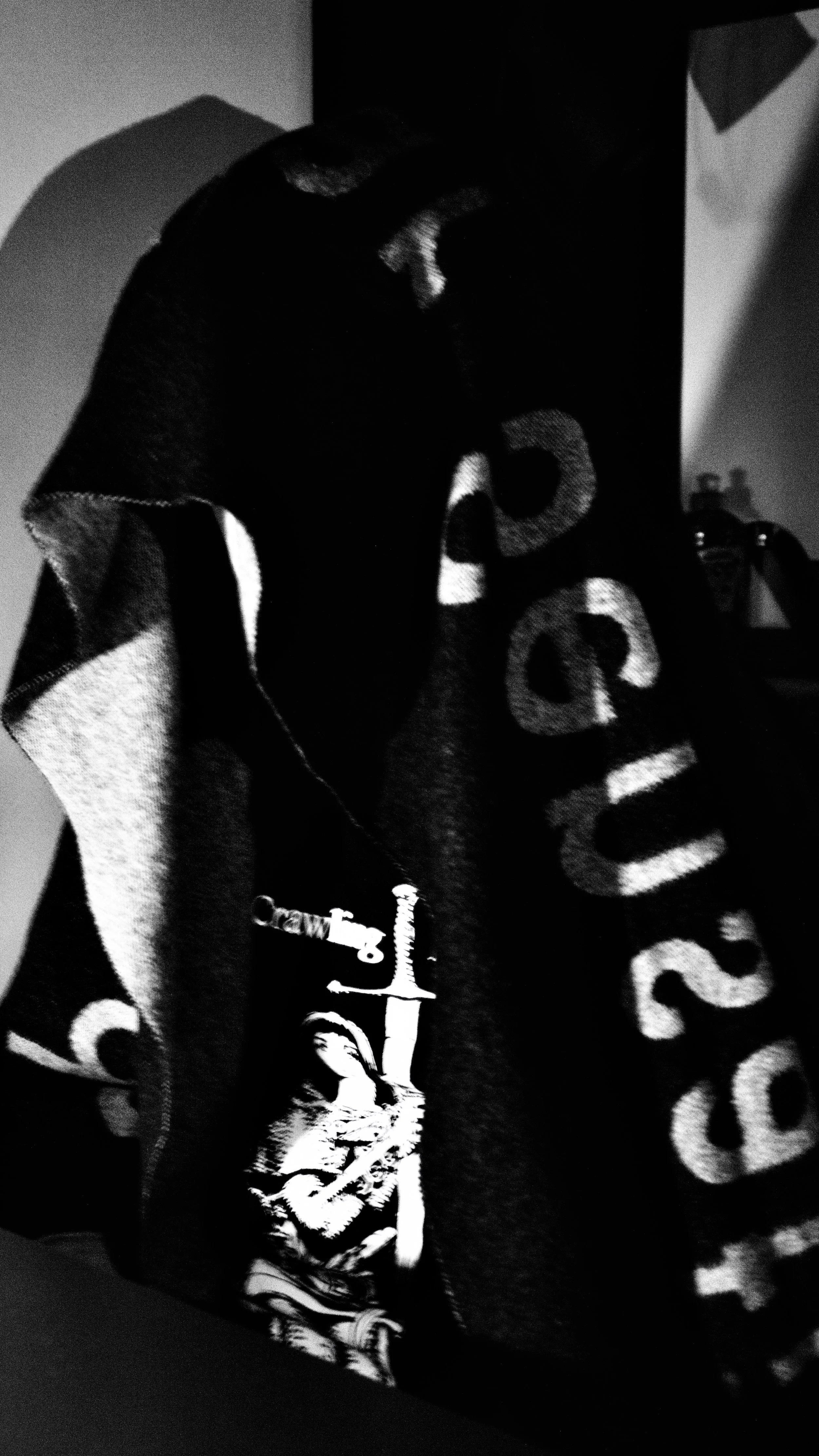 A black and white image of a fabric with bold letters and a graphic of a woman holding a rifle.