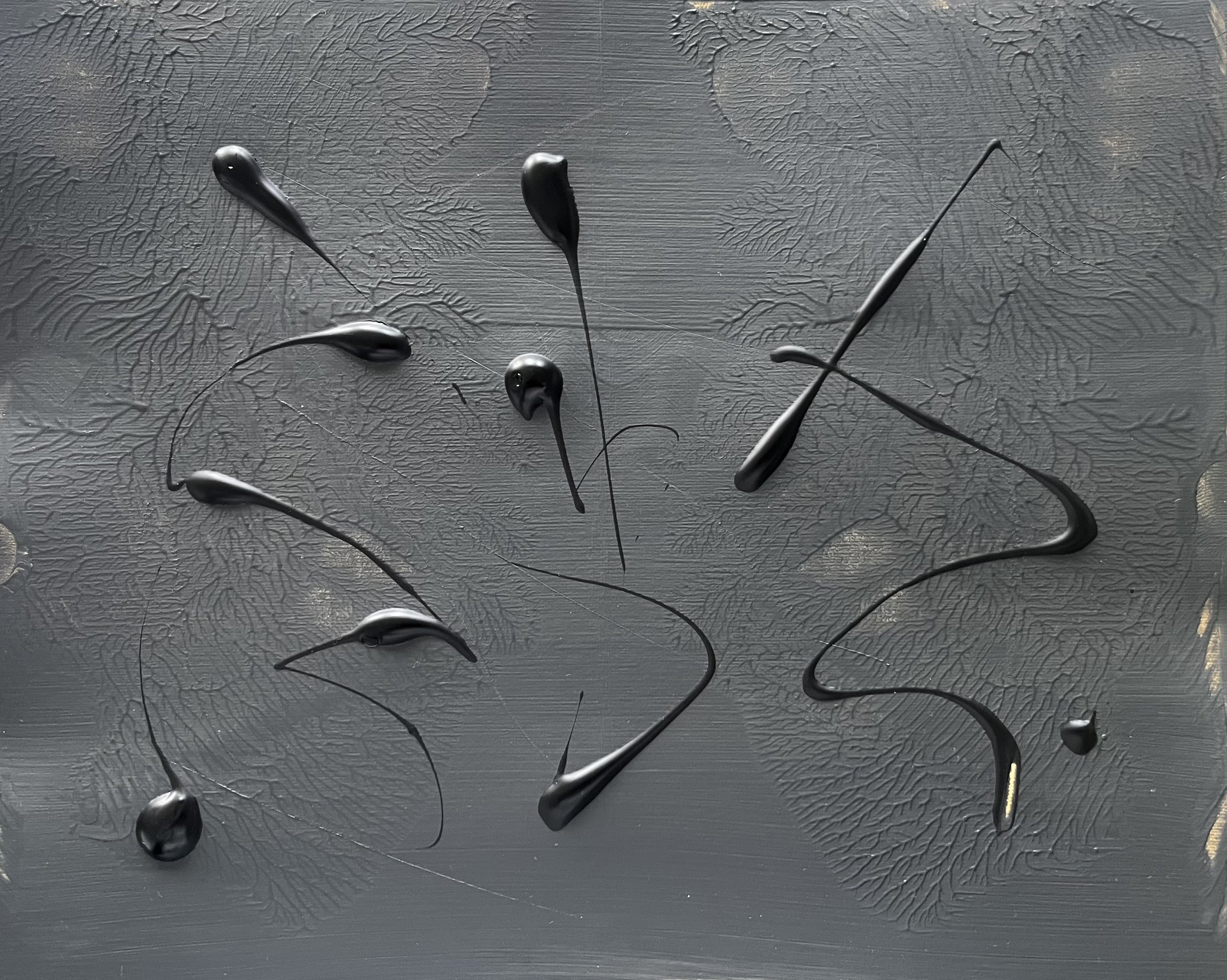 Close-up of black liquid droplets on a textured gray surface.