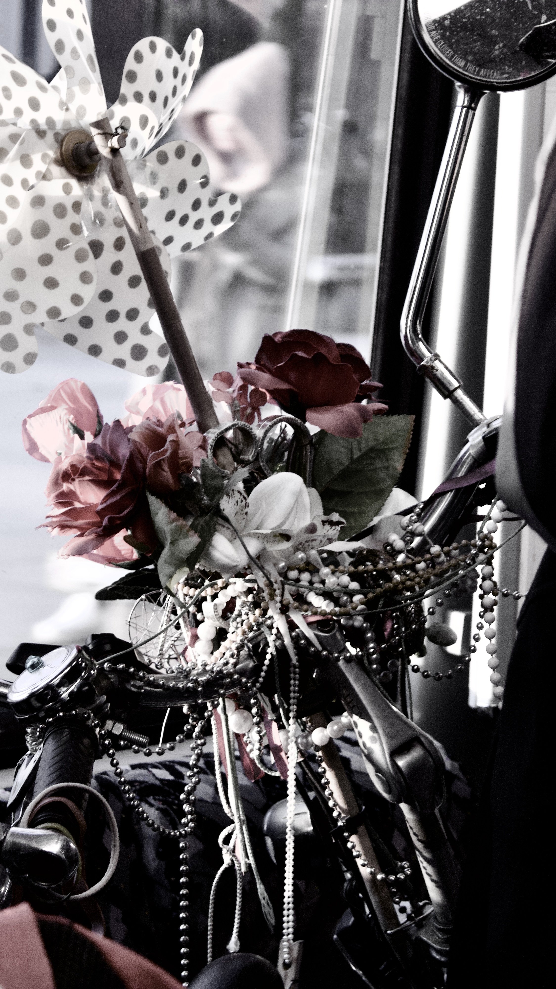 Close-up of a bicycle decorated with flowers, pearl necklaces, and ribbons, with a reflection of a person in the background.