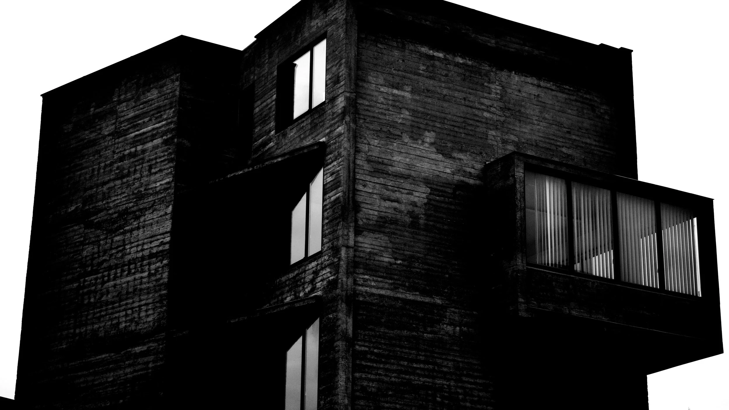 Black and white photo of a modern building with multiple windows, some with blinds, and textured exterior walls.