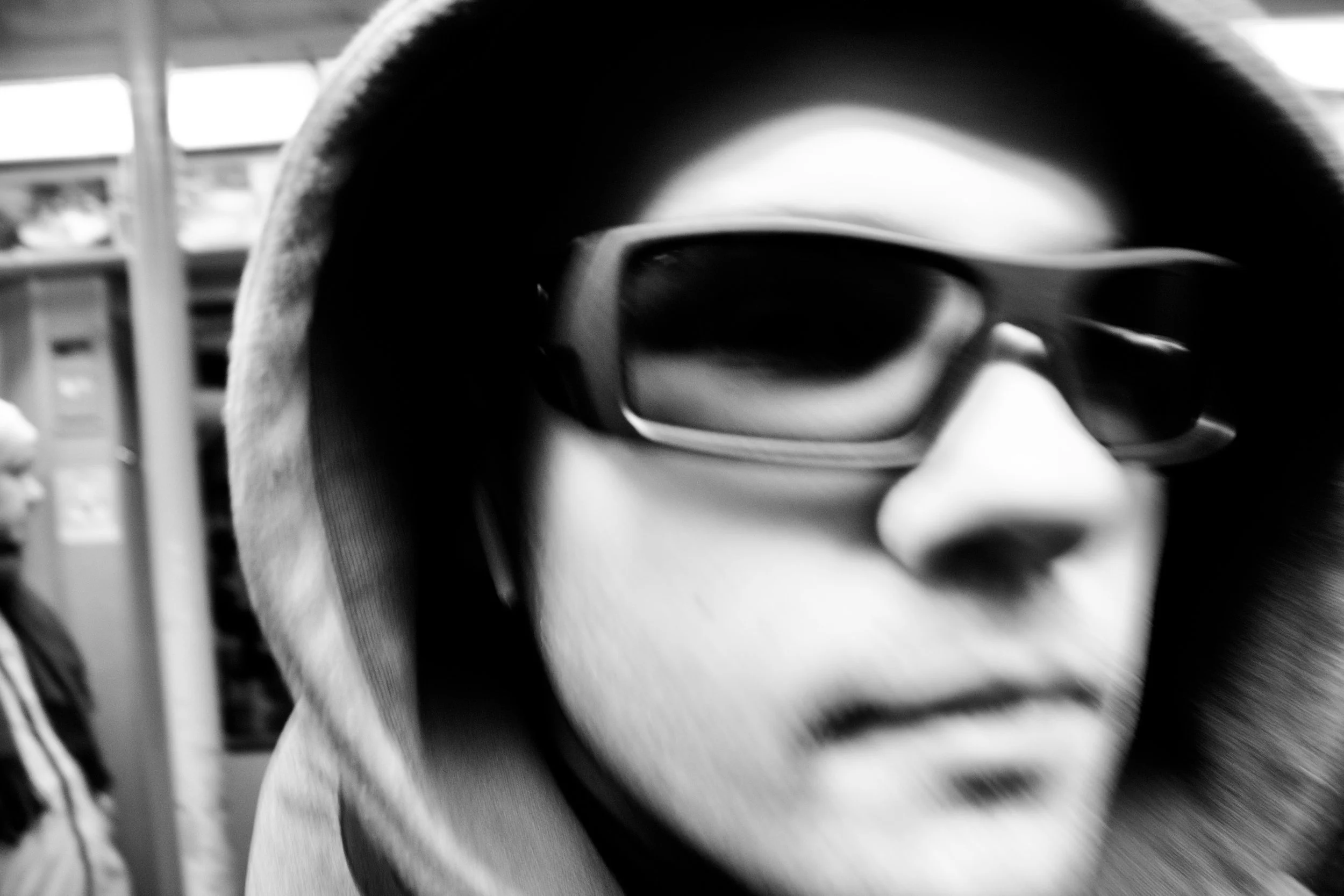 Close-up of a person's eye wearing dark sunglasses, with part of the face covered by a hoodie, inside a vehicle.