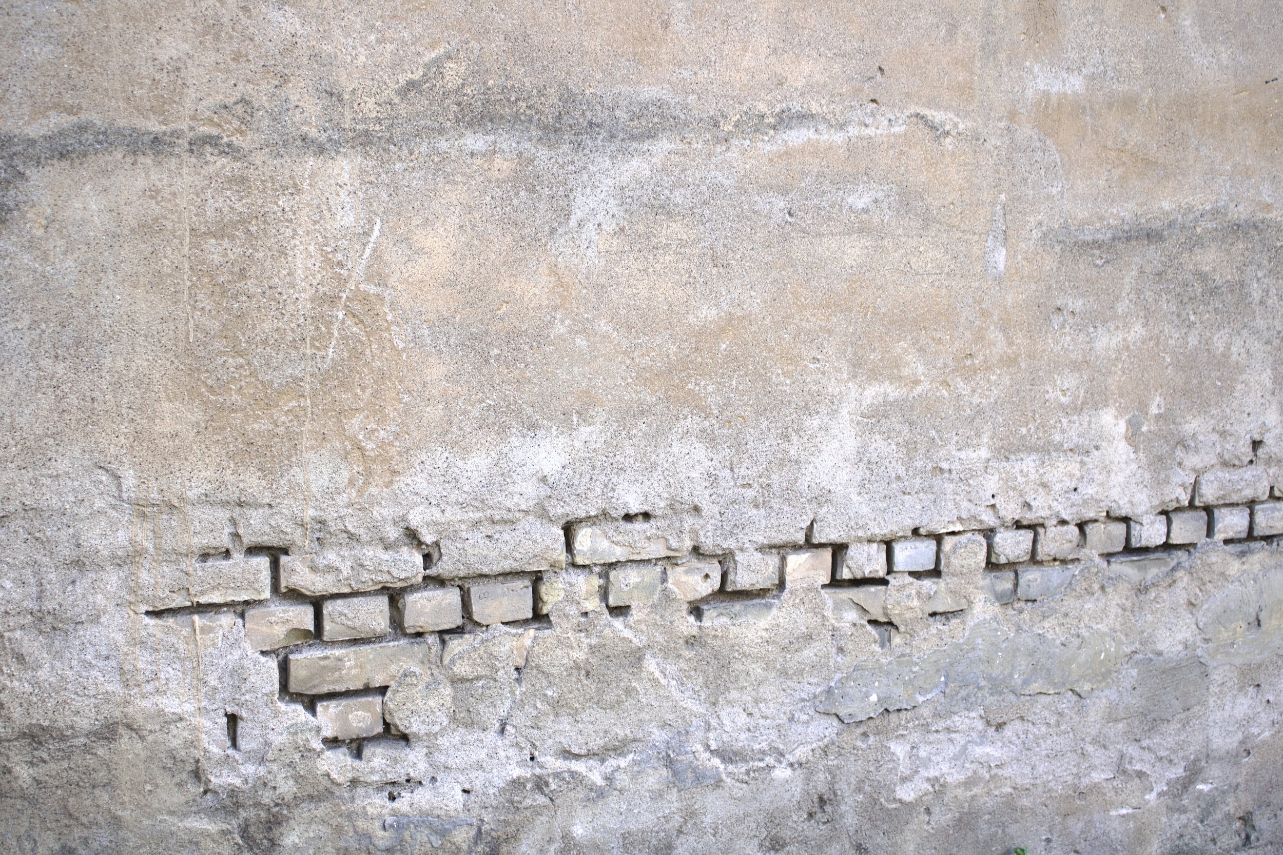 Close-up of a weathered beige brick wall with some mortar cracks and uneven surface textures.