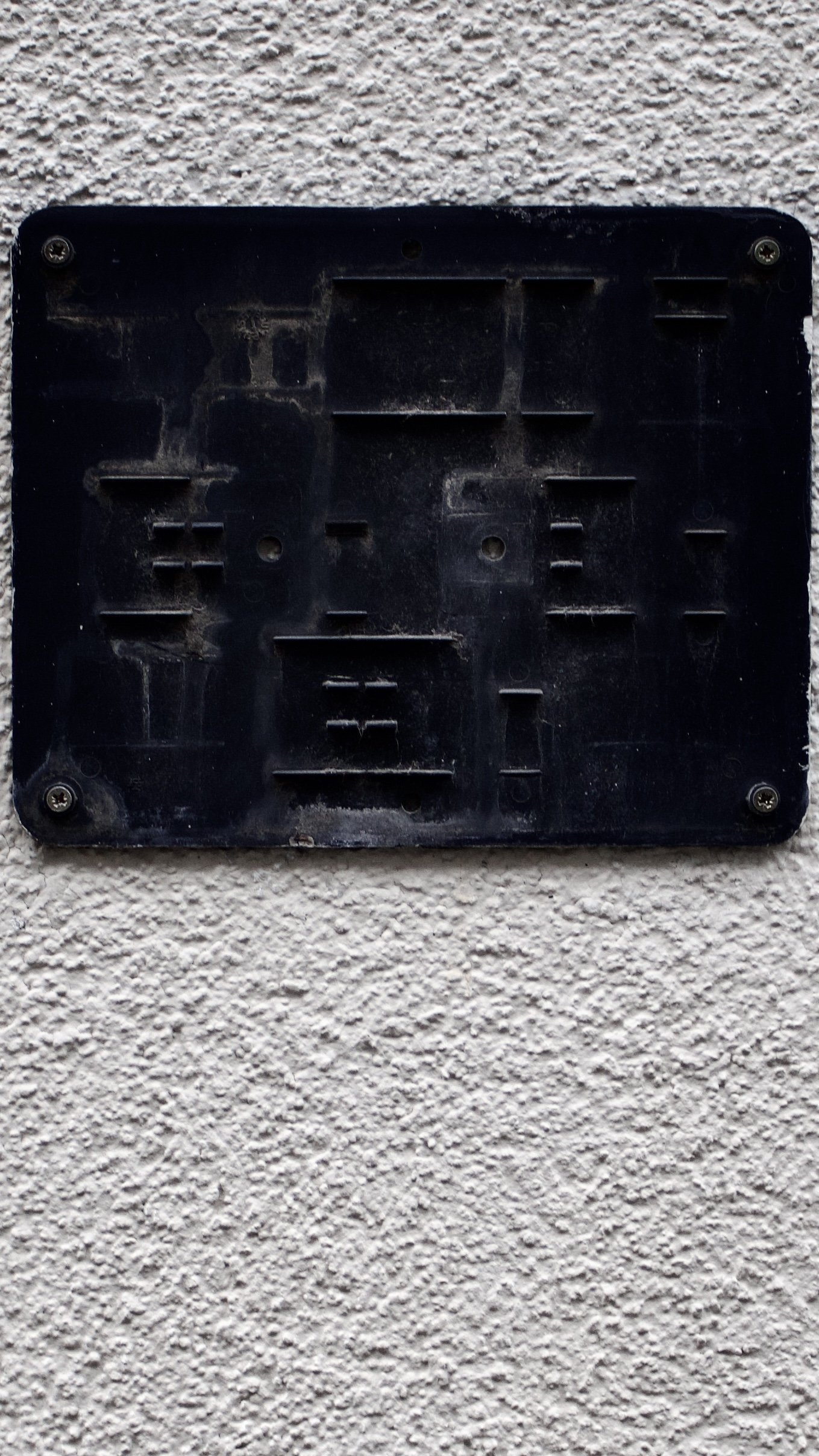 A black, empty electronic device outlet cover mounted on a textured off-white wall.