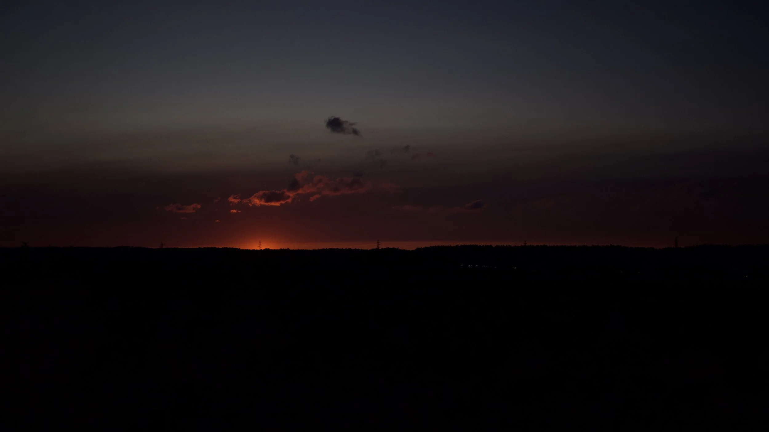 Sunset over a dark horizon with a few clouds and a gradient sky ranging from dark blue to orange near the horizon.