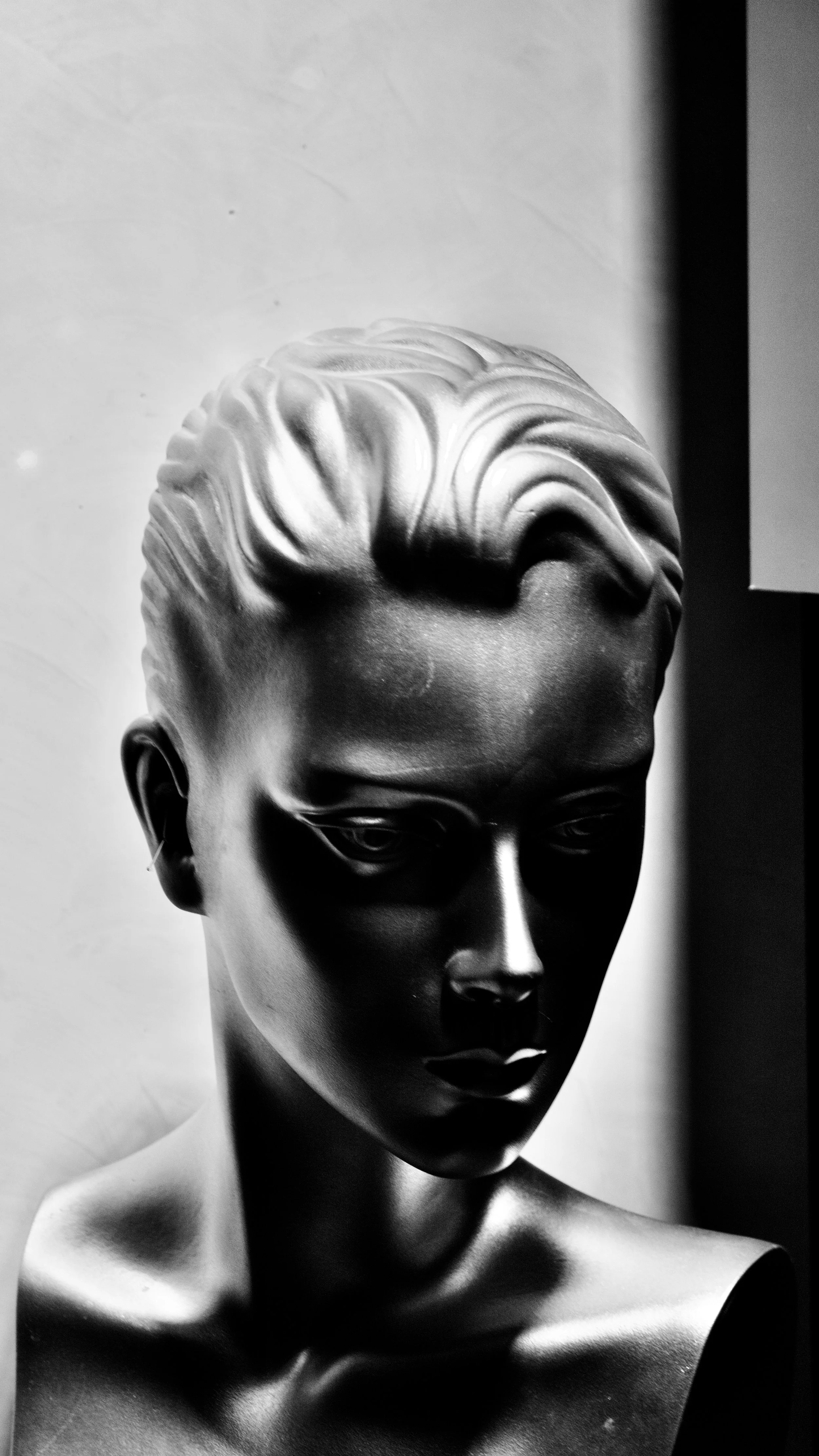 Black and white photo of a female mannequin head with styled hair, focused on the face and upper shoulders.