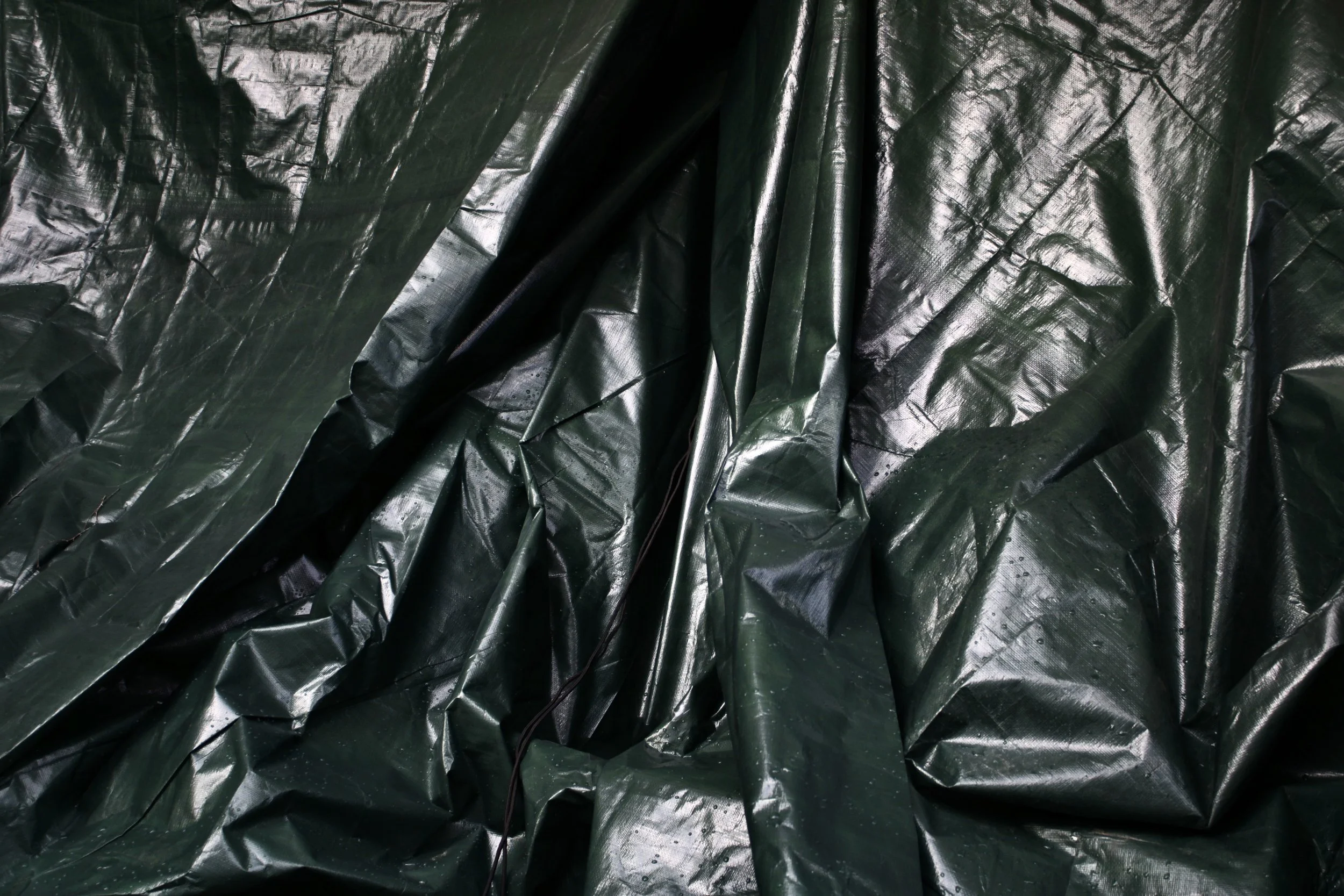Dark green, shiny plastic tarp with visible creases and folds.