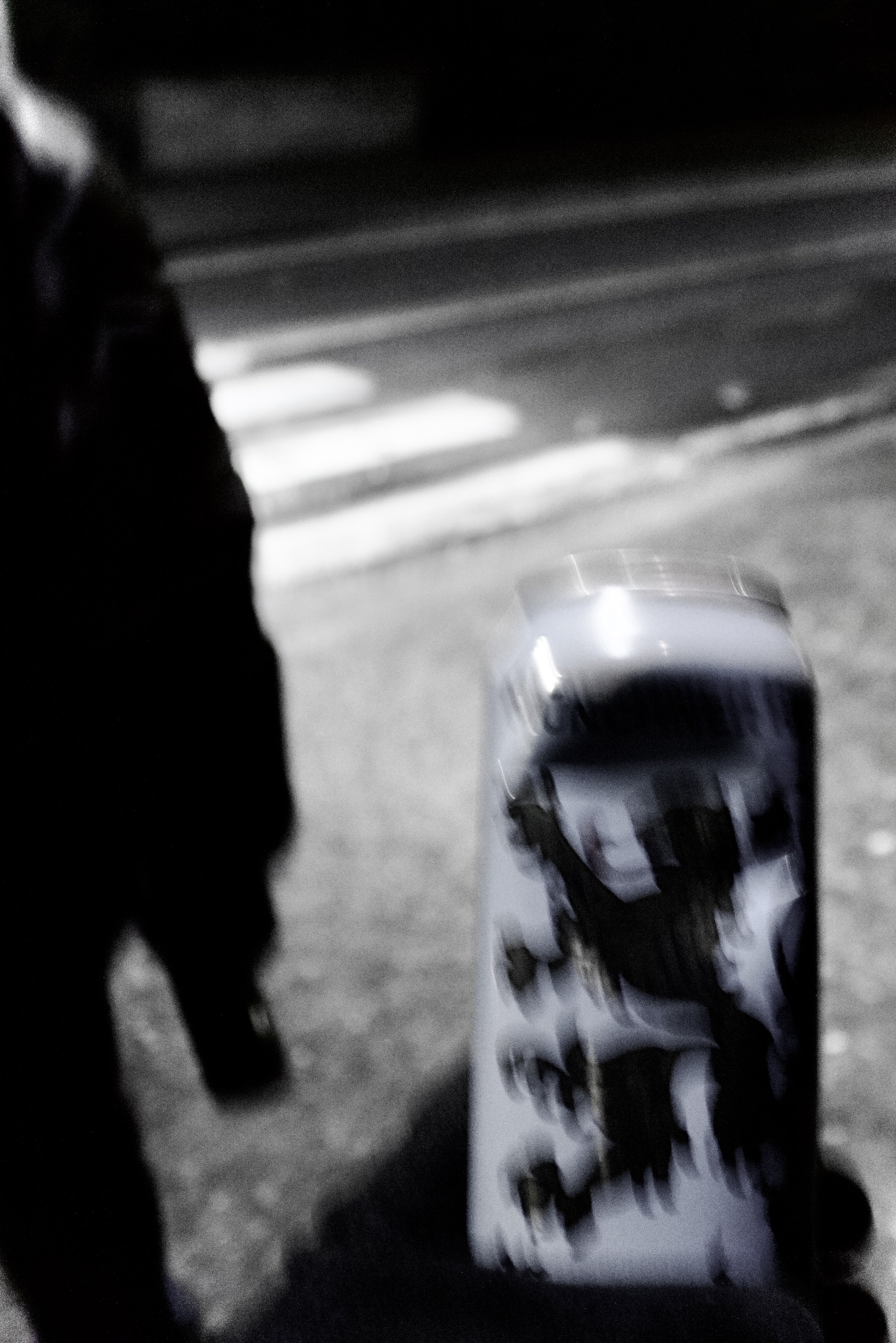 Close-up of a clear plastic bottle lying on a surface with a white label that has black text, and a dark-colored object or shadow partially covering it, with background of a smooth, reflective surface.