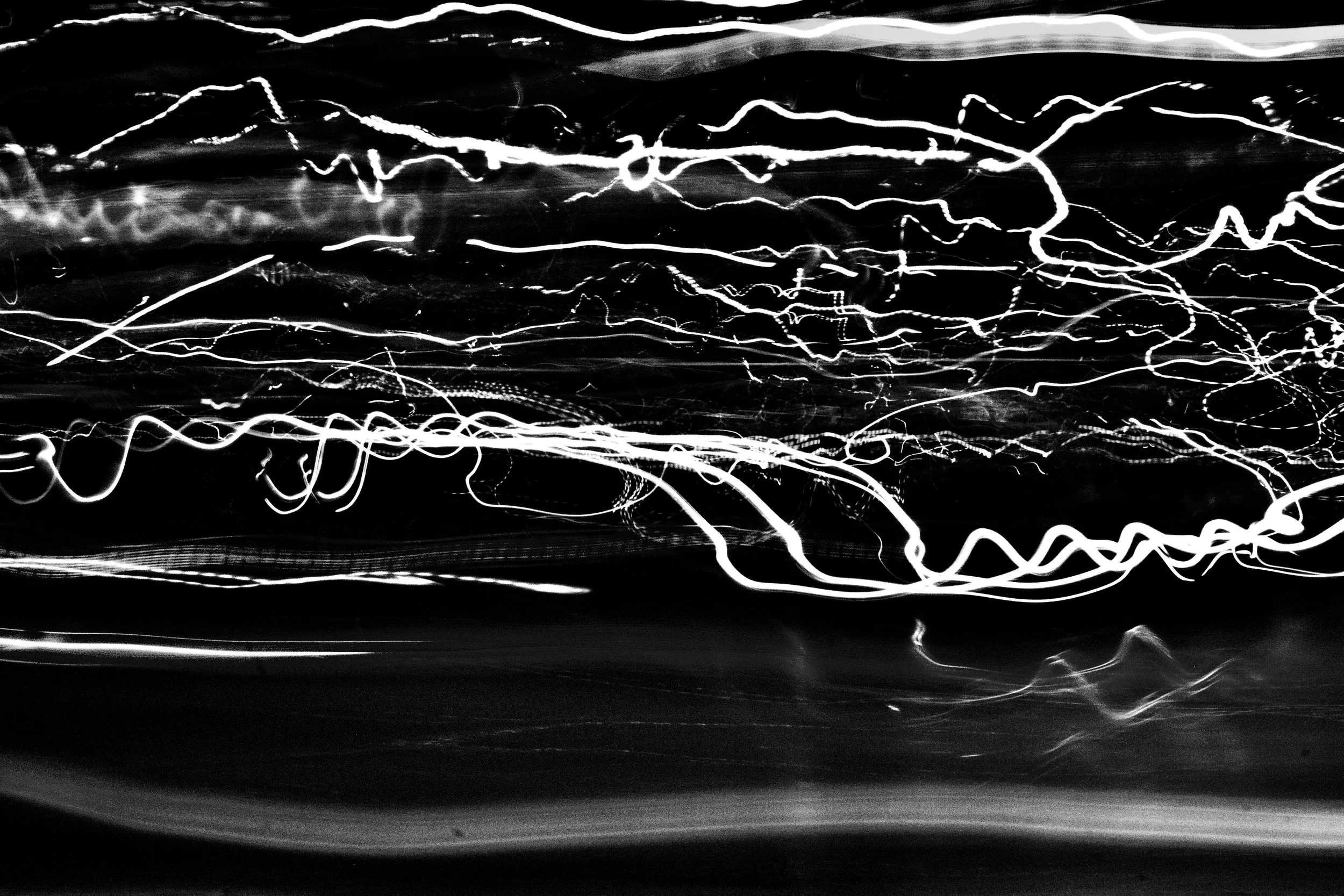 Black and white long-exposure photograph of light trails across the scene, creating abstract, wavy lines.