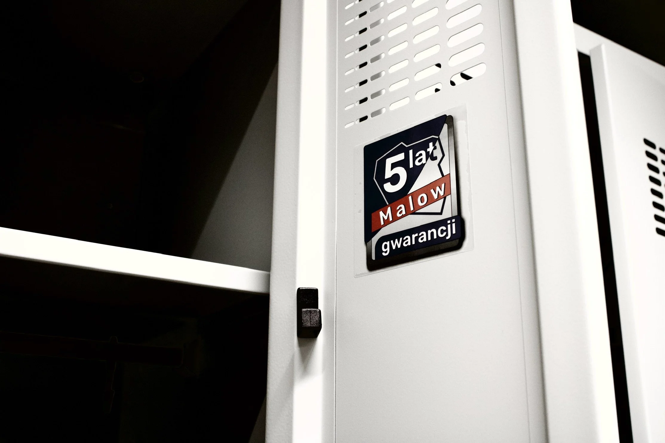 Close-up of a white locker with a sticker that reads '5 lat Młow gwarancji'.