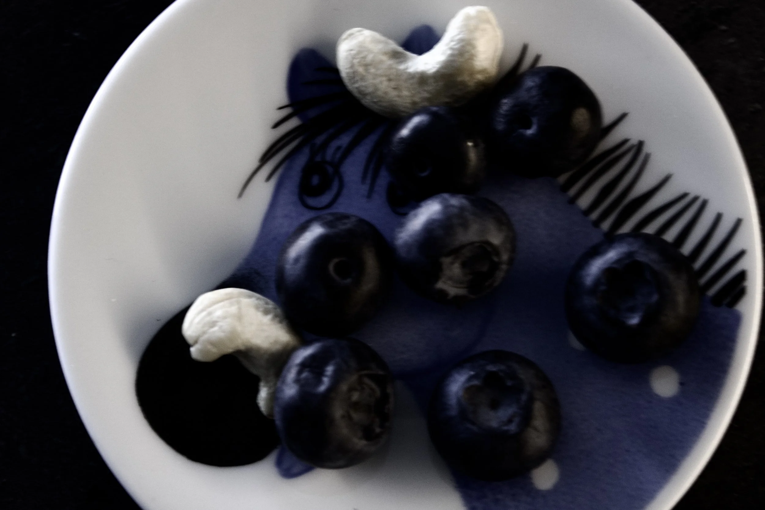 A white bowl filled with blueberries and a couple of almonds.